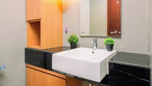 Un baño con lavamanos blanco, armarios de madera, un espejo y dos plantas en macetas.