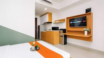 A modern hotel room with a bed, a TV mounted on the wall, a kitchen area, and a small refrigerator.