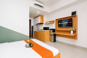 Quarto de hotel moderno com cama, televisão fixada na parede, área de cozinha e um pequeno frigorífico.