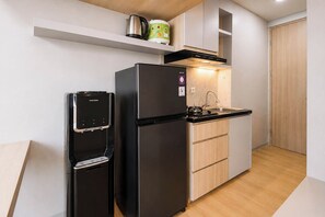 Eine kompakte Küche mit einem schwarzen Kühlschrank, einem Wasserspender, einem Herd und Holzschränken.