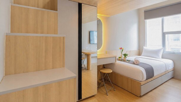 A modern bedroom with a bed, bedside table, and a desk area. - Stylish And Warm Studio At Apartment The City Square Surabaya (Surabaya)