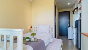 A hotel room with two beds, a small table with a vase of flowers, and a kitchenette area. - Urban Minimalist Studio At Apartment Tamansari Papilio (Surabaya)