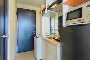 A compact kitchen with a microwave, refrigerator, and a small washing machine. - Urban Minimalist Studio At Apartment Tamansari Papilio (Surabaya)