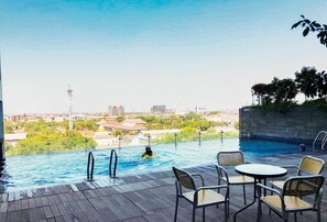 Ein Pool im Freien mit Blick auf eine Stadtlandschaft, umgeben von Liegestühlen und einer Holzterrasse.