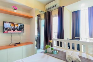 Habitació d'hotel amb un llit, una televisió penjada a la paret, una finestra amb cortines i una petita planta sobre la taula de nit.