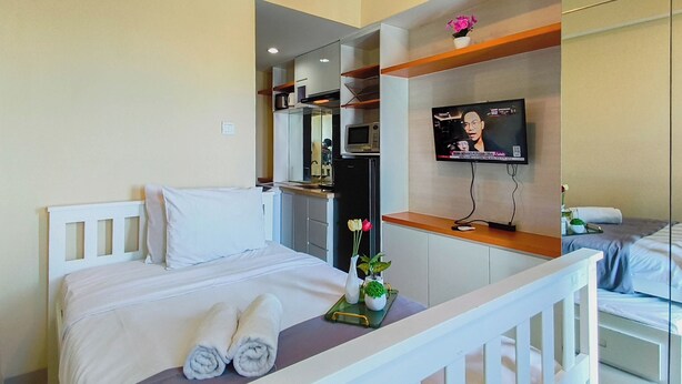 A hotel room with a bed, a TV, a small table with a vase of flowers, and a microwave. - Urban Minimalist Studio At Apartment Tamansari Papilio (Surabaya)