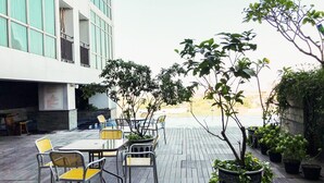 An outdoor seating area with tables and chairs, surrounded by potted plants and trees. - Urban Minimalist Studio At Apartment Tamansari Papilio (Surabaya)