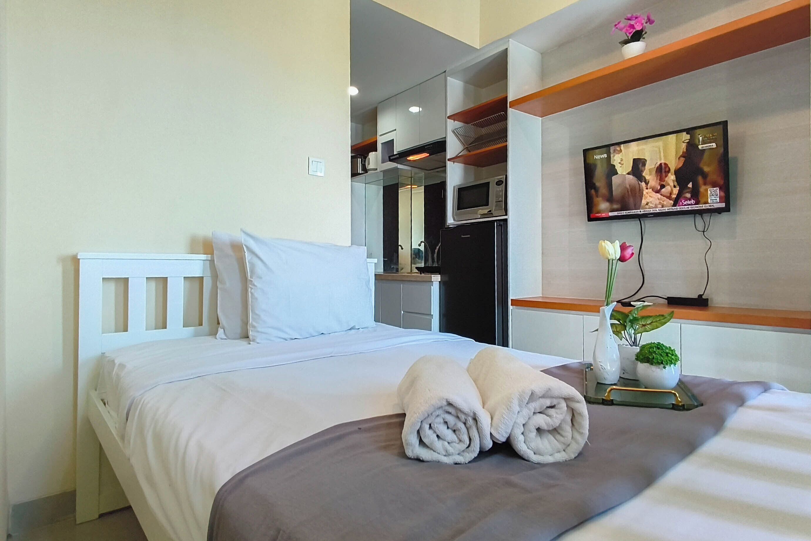 A hotel room with a bed, a flat-screen TV mounted on the wall, a small table with a vase of flowers, and a microwave above the table.