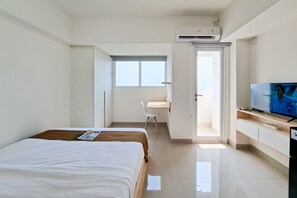 A hotel room with a bed, a desk, a television, and an air conditioning unit. - Comfortable Nice Studio Room At Apartment Cisauk Point (Cisauk)