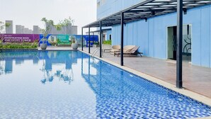 A swimming pool with tiled flooring, a covered seating area, and a building with a blue exterior. - Comfortable Nice Studio Room At Apartment Cisauk Point (Cisauk)