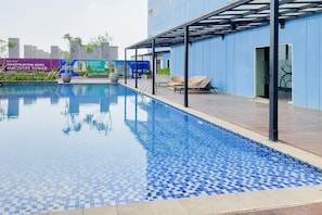 A swimming pool with tiled flooring, a covered seating area, and a building with a blue exterior. - Comfortable Nice Studio Room At Apartment Cisauk Point (Cisauk)