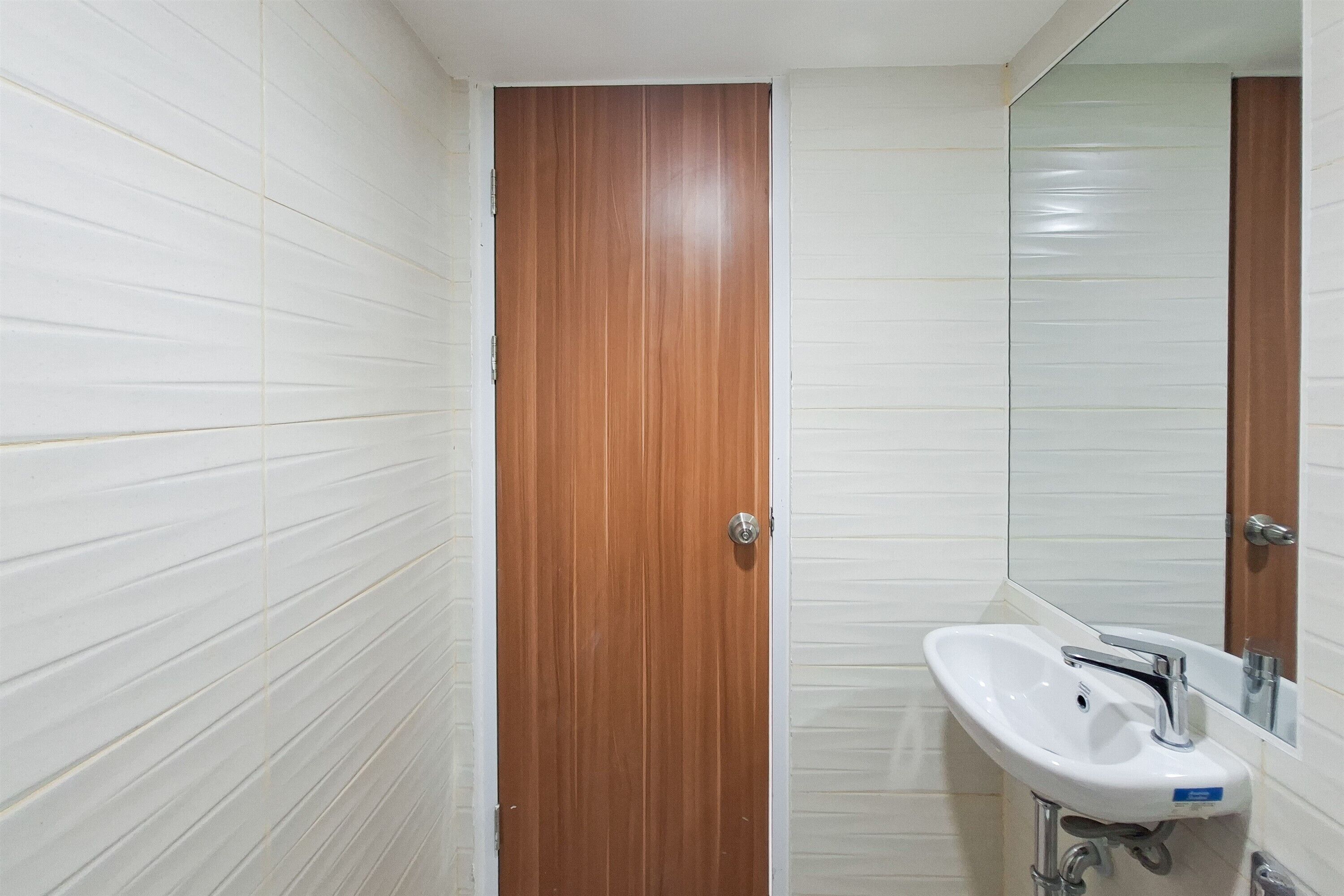 A bathroom with white tiled walls, a wooden door, and a white sink with a mirror above it.