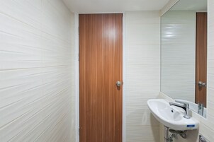 A bathroom with white tiled walls, a wooden door, and a white sink with a mirror above it.