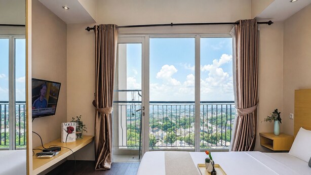 Quarto de hotel com uma cama grande, televisão em um suporte, escrivaninha com computador e varanda com vista para a cidade.