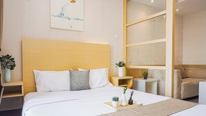 Quarto de hotel com cama, mesas de cabeceira, uma cadeira, uma mesinha com um vaso e planta, e uma obra de arte na parede.