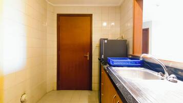 A small bathroom with a wooden door, a sink, a mirror, and a black refrigerator.
