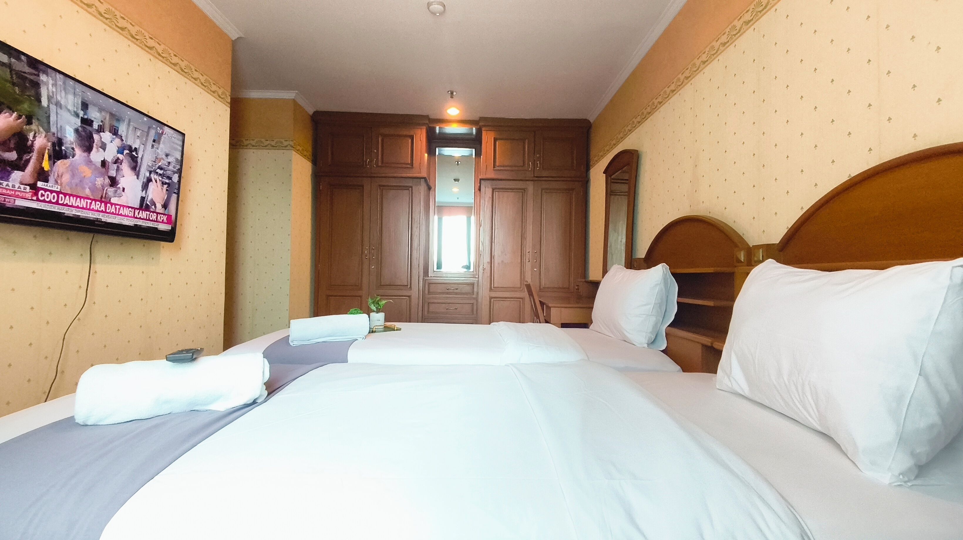 A hotel room with a large bed, a television mounted on the wall, and wooden furniture.