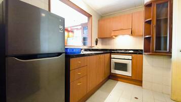 A compact kitchen with a refrigerator, oven, and wooden cabinets.