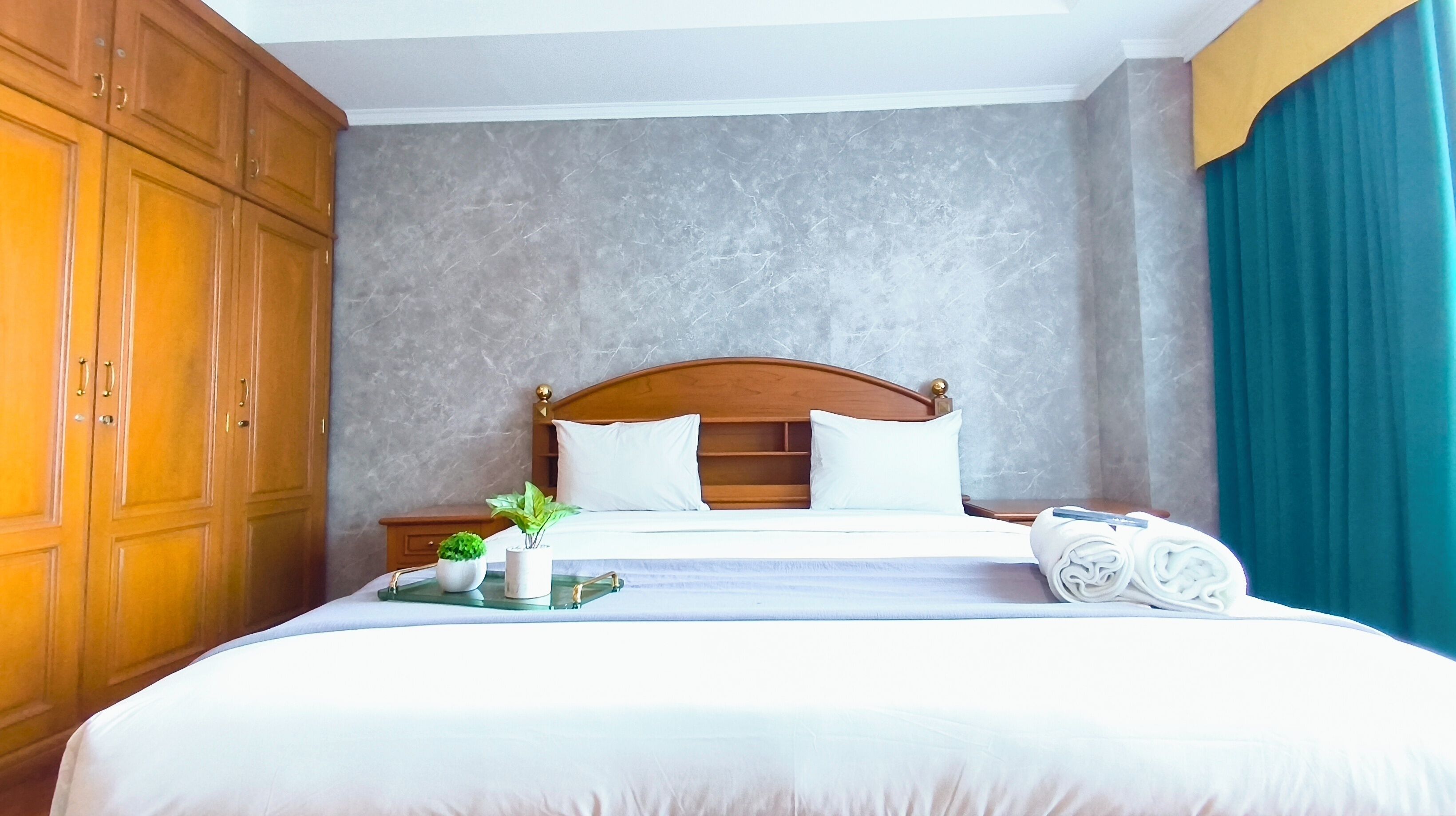 A hotel room with a large bed, wooden headboard, and a nightstand with a plant.
