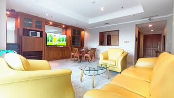 A living room with yellow sofas, a glass coffee table, wooden cabinets, a television, and a dining area with chairs and a table.