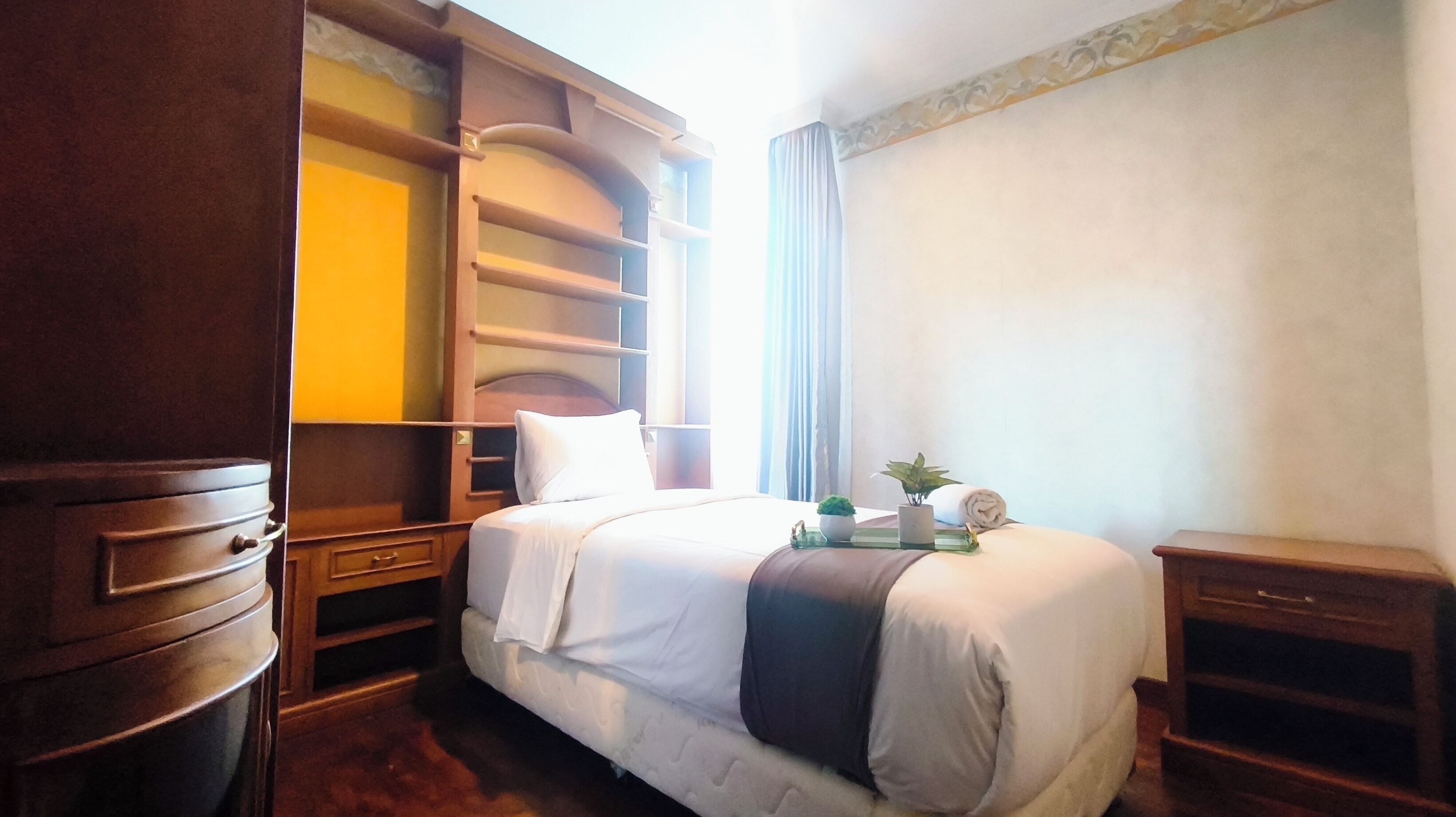 Ein Hotelzimmer mit Bett, Nachttisch, Kommode und einem Fenster mit Vorhängen.