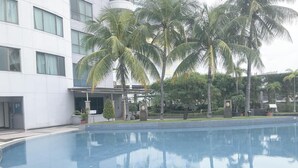Ein Swimmingpool mit einer Fliesenbordsteinkante, umgeben von Palmen und einem Gebäude mit mehreren Fenstern.