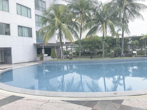 Ein Swimmingpool mit einer Fliesenbordsteinkante, umgeben von Palmen und einem Gebäude mit mehreren Fenstern.
