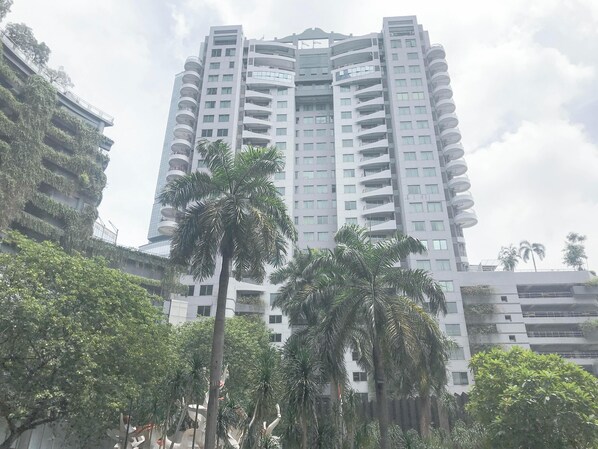 A high-rise building with multiple balconies, surrounded by greenery and other buildings.
