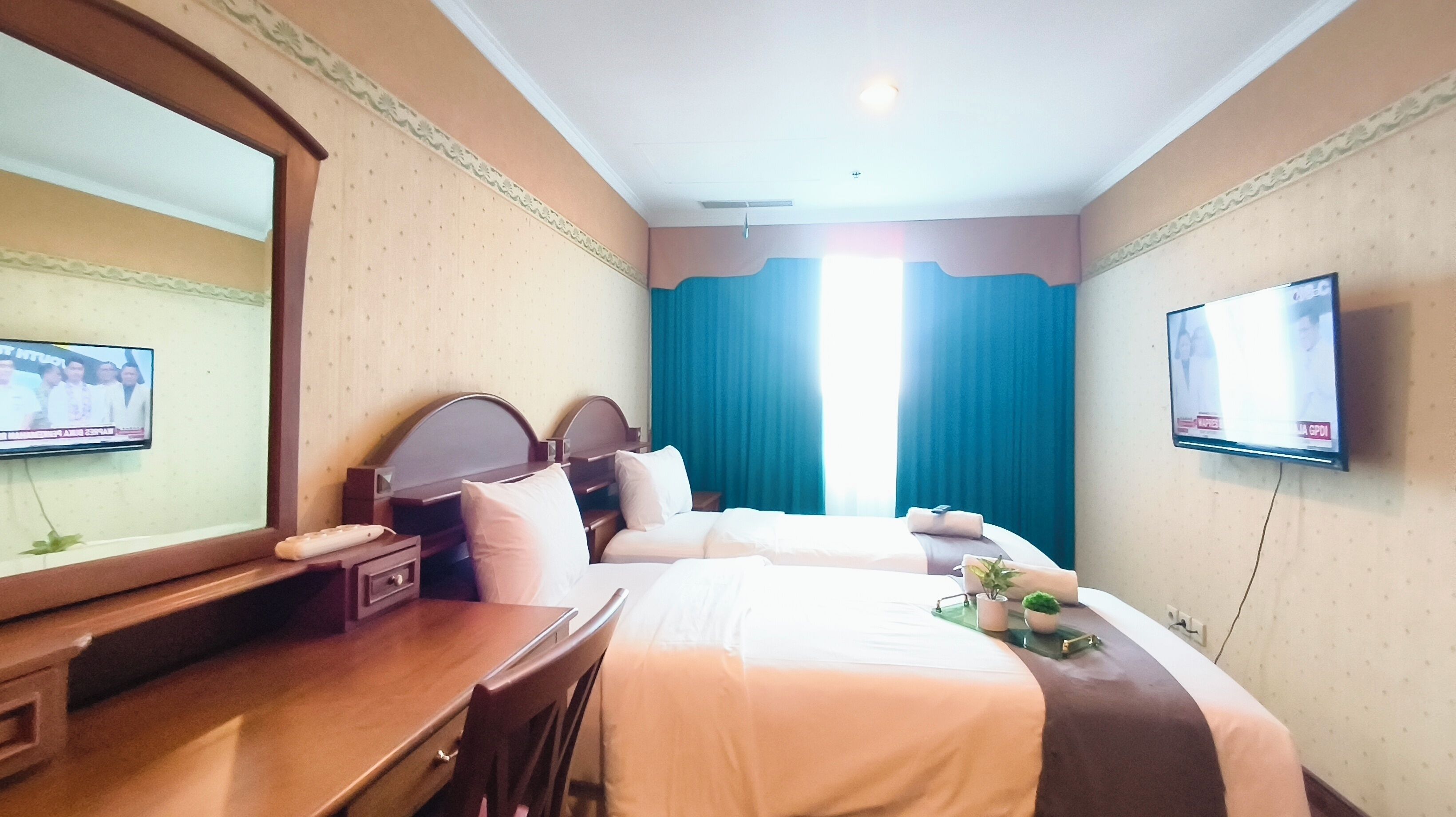 A hotel room with two beds, a desk, a TV, and a large mirror.