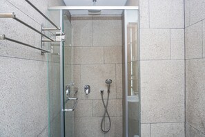 En moderne bruser med glasdør, håndbruser og vandhane på væggen.
