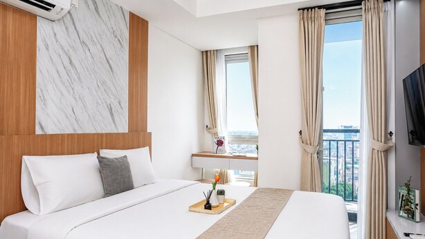 A hotel room with a bed, a desk, a chair, a TV, and a window with curtains. - Studio Bright Areum Residence At Antasari Place (Jakarta)