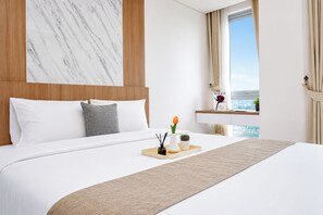 Et hotelværelse med en stor seng, en marmorvæg, et træhovedgærde, et vindue med udsigt og et natbord med en vase blomster.