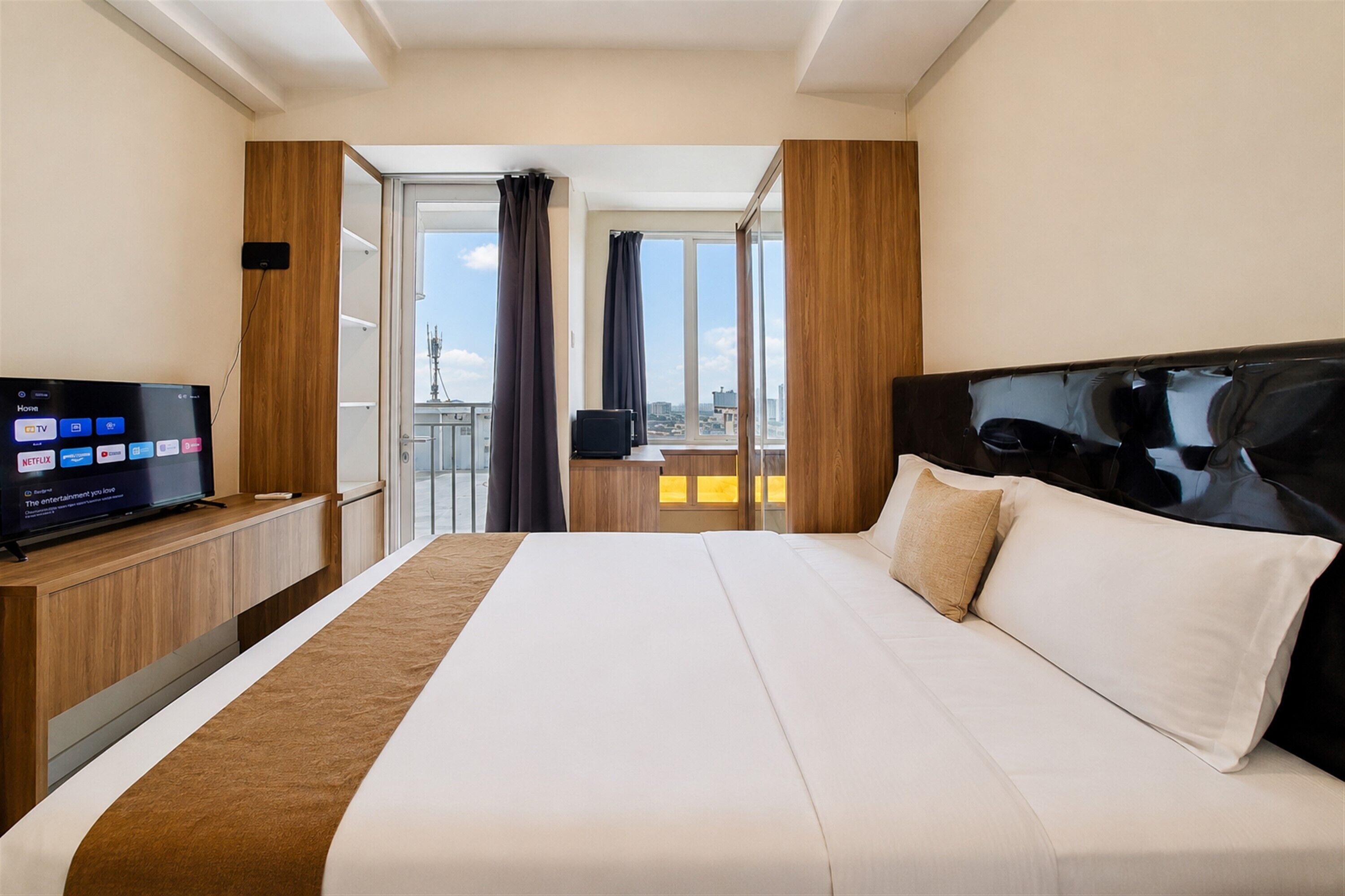 A hotel room with a large bed, a TV on a wooden stand, and a view of the city through the window.