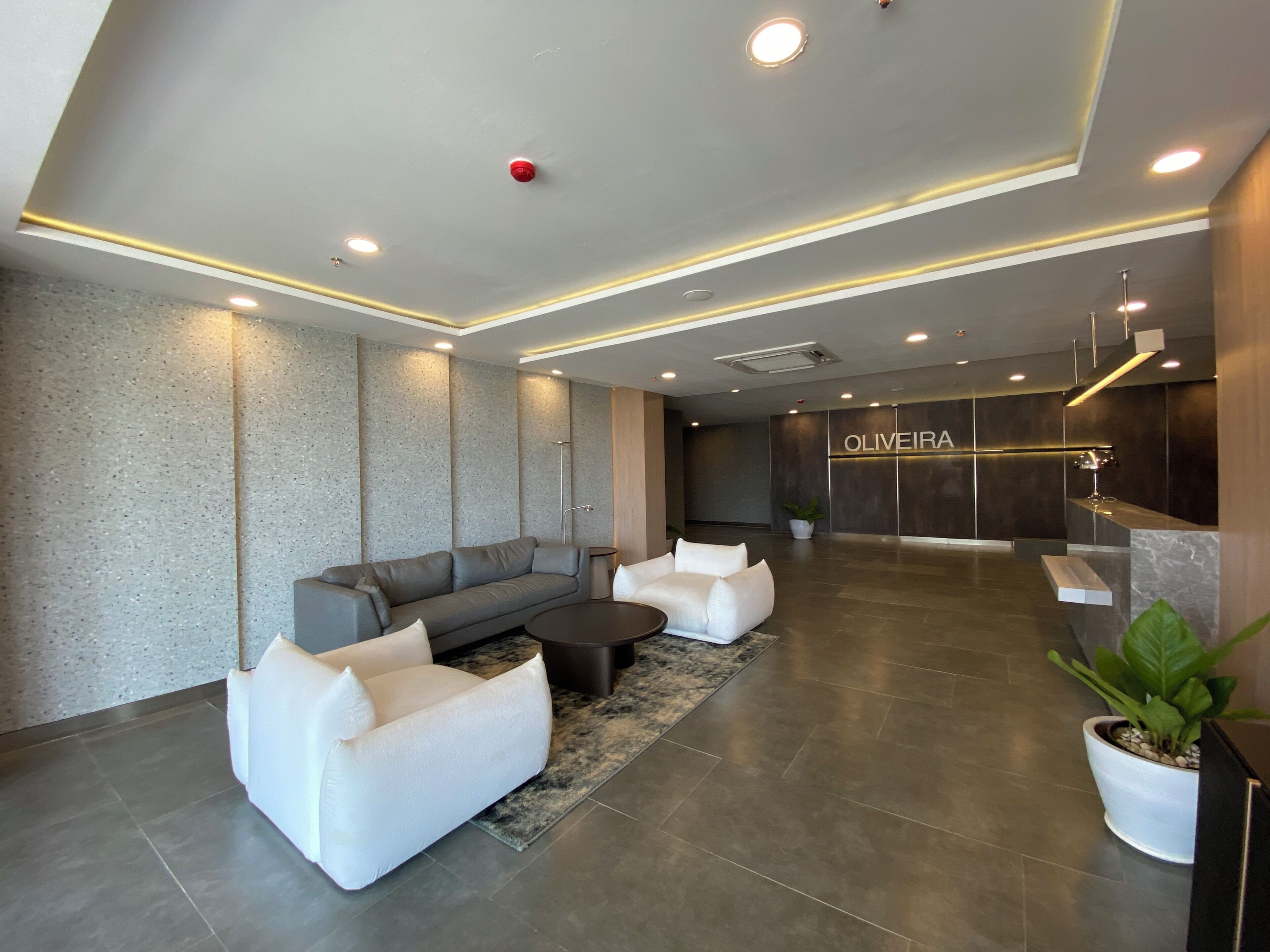 Un vestíbulo moderno con un sofá gris, sillones blancos, una mesa de centro y un mostrador de recepción.