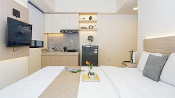 Habitación de hotel compacta con cama, mesita de noche, una pequeña kitchenette y un televisor montado en la pared.