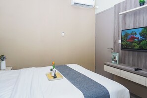 A hotel room with a bed, a television mounted on the wall, a small table with a plant, and a window. - Trendy 2Br At Apartment Vasanta Innopark (Cikarang)