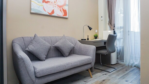 A modern living room with a grey sofa, a desk, a chair, and a large abstract painting on the wall. - Trendy 2Br At Apartment Vasanta Innopark (Cikarang)