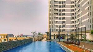 A swimming pool with a view of a high-rise building in the background. - Trendy 2Br At Apartment Vasanta Innopark (Cikarang)