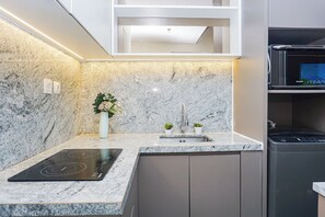 Una cocina moderna con placa de inducción integrada, horno de acero inoxidable y salpicadero de mármol.