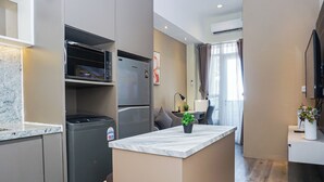 A modern kitchen with a built-in refrigerator, microwave, and oven. There's a small island with a potted plant. - Trendy 2Br At Apartment Vasanta Innopark (Cikarang)