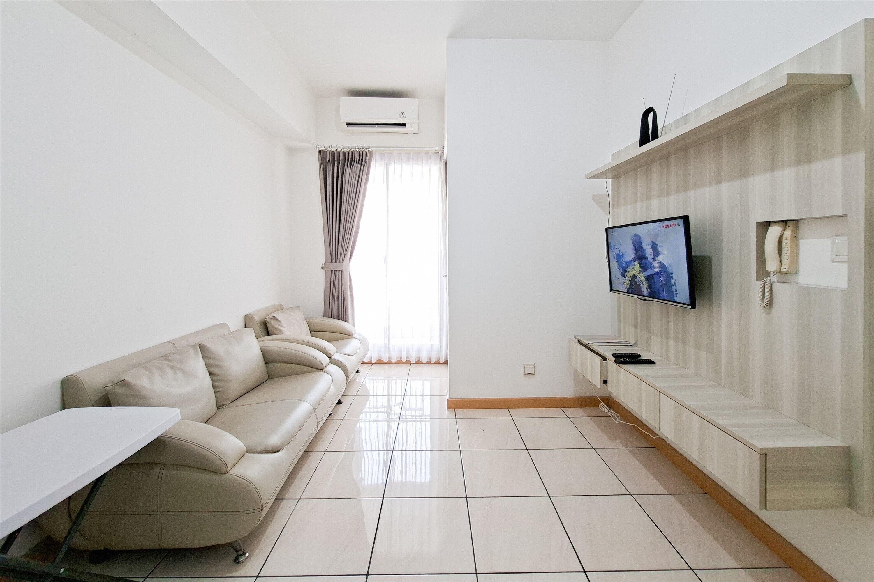 A modern living room with a sofa, a flat-screen TV, a small table, and a built-in shelf with a telephone.