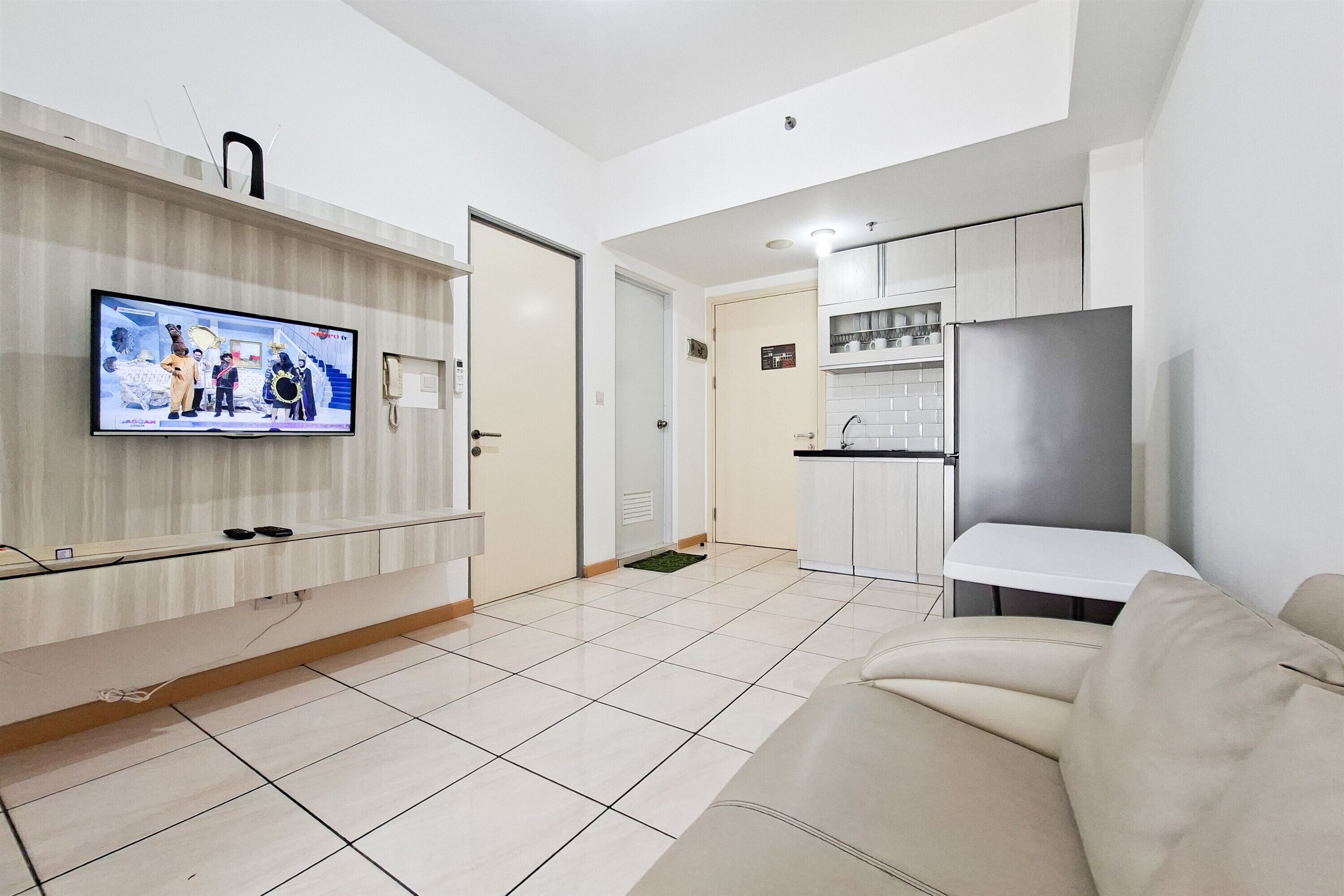 Una sala moderna con una televisión de pantalla plana montada en la pared, un sofá y una cocina con armarios y un refrigerador.