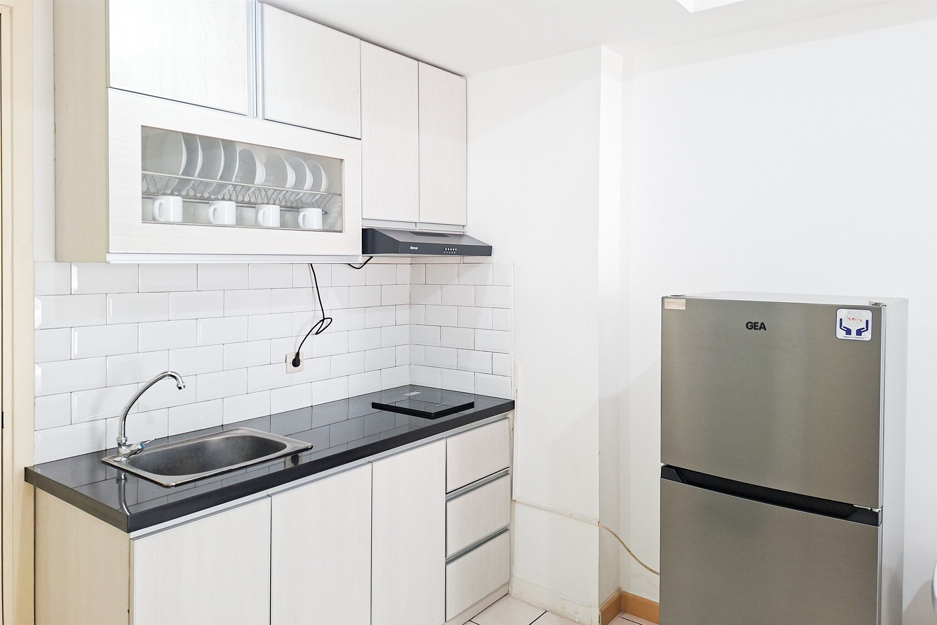 A compact kitchen with white cabinets, a stainless steel refrigerator, a black countertop, and a built-in dishwasher.