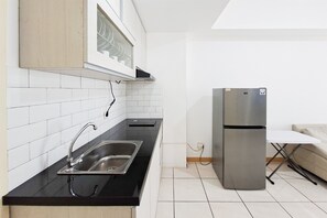 Cozinha moderna com pia de aço inoxidável, bancada preta, azulejos brancos e geladeira embutida.