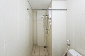 Et lille badeværelse med hvide fliser, en bruseniche og et toilet.