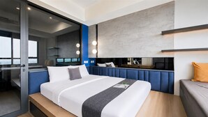 A modern hotel room with a large bed, a glass door leading to a balcony, and a built-in vanity with lights. - Fully Furnished 1Br At Apartment Collins Boulevard (Tangerang)
