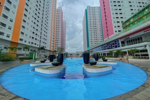 Piscina com uma fonte central, rodeada por edifícios altos com varandas.