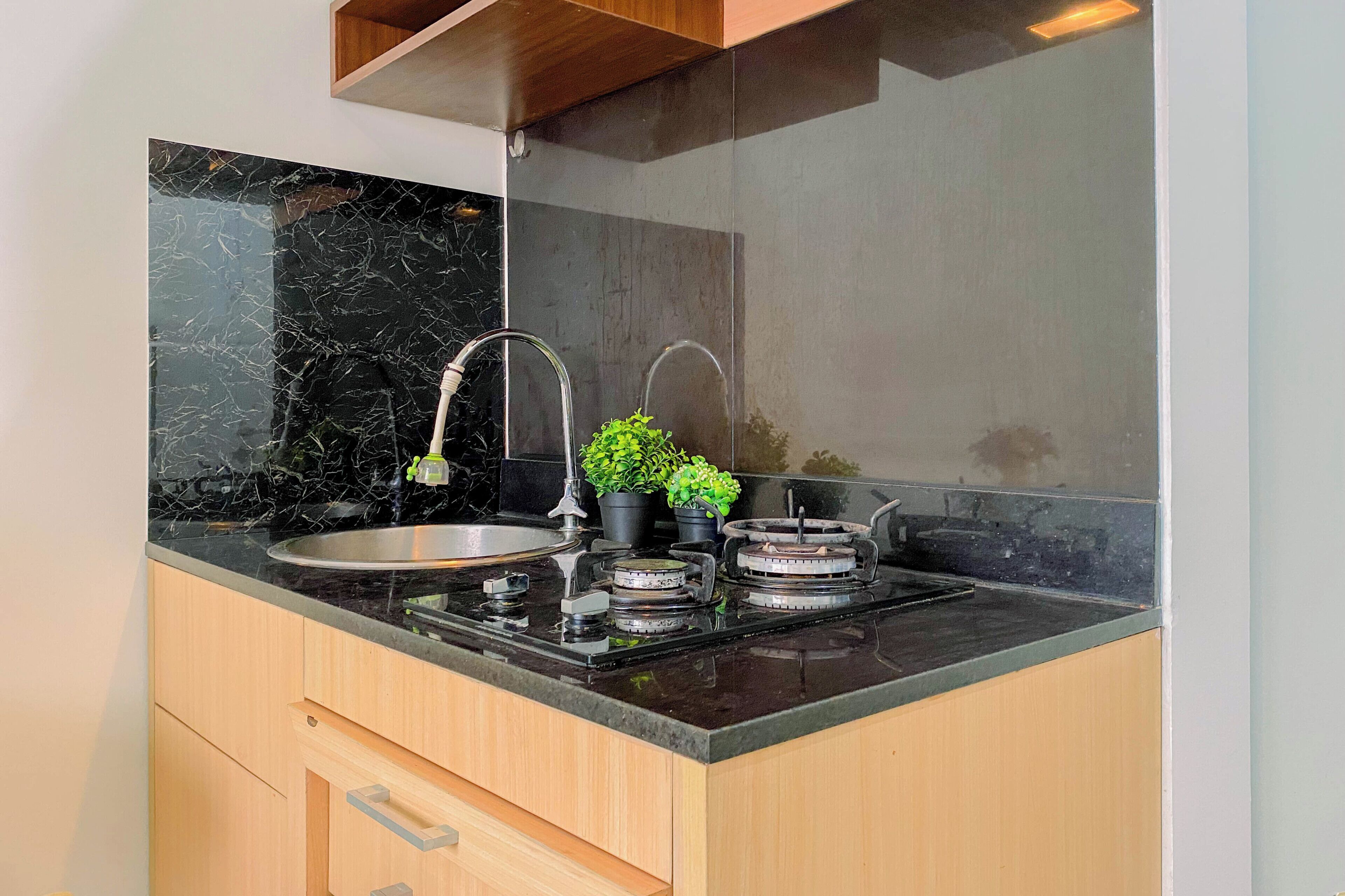 Una cocina con encimera de mármol negro, pileta de acero inoxidable, cocina a gas y una pequeña planta en maceta.
