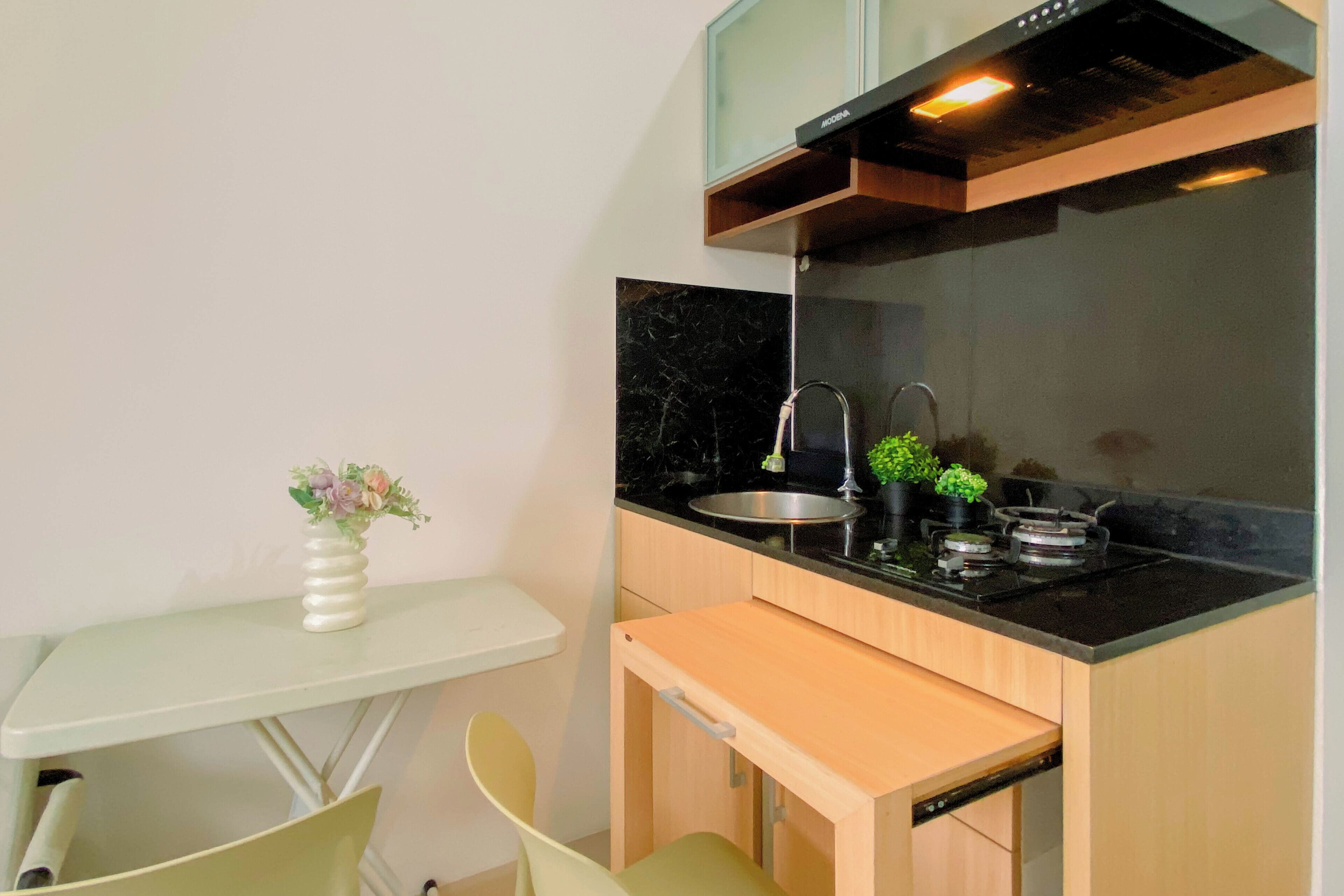Cozinha compacta com bancada preta, pia de aço inoxidável e um pequeno espaço de refeições com mesa branca e duas cadeiras.