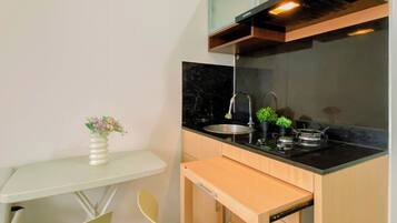 Cozinha compacta com bancada preta, pia de aço inoxidável e um pequeno espaço de refeições com mesa branca e duas cadeiras.